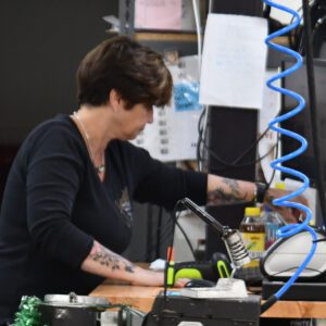 Lab manager Susan focused on her task at a workbench with tools and equipment in a workshop setting.